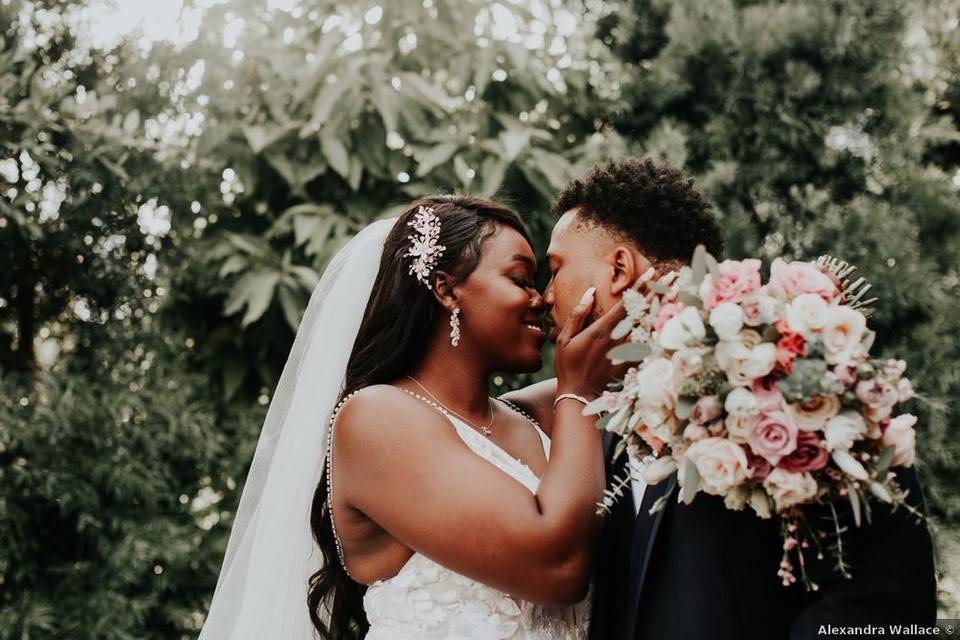 Black couple looks into each other's eyes while smiling. The bride is wearing a veil and has her hand on his cheek