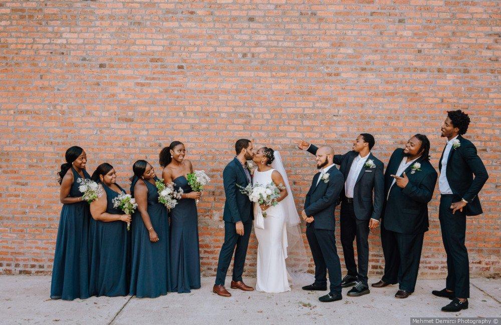 Newlyweds kissing with both sides of wedding party standing on either side and bridesmaids wearing navy