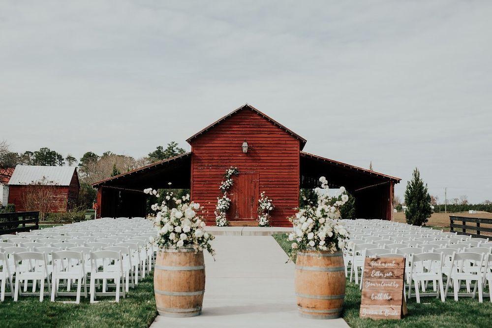 rustic outdoor wedding aisle decor flower arrangements on top of wine barrels on both sides of the aisle