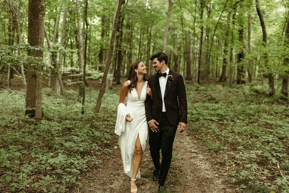 bride and groom walking arm in arm in the woods