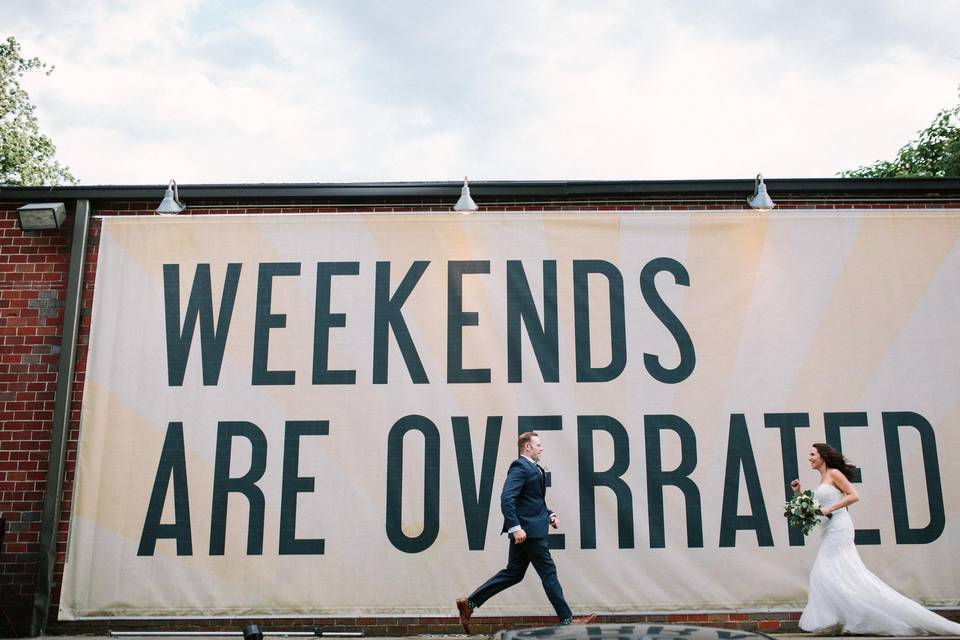 bride and groom walking in front of billboard that says weekends are overrated