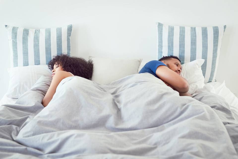 couple laying back to back in bed with striped pillows behind them