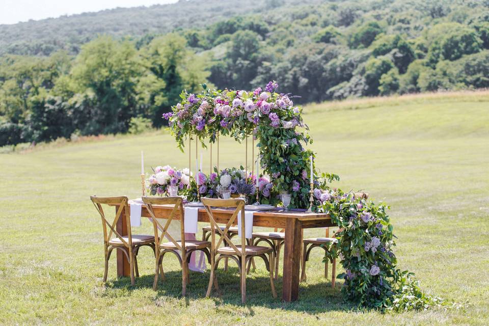 small outdoor wedding reception table decorated with purple and greenery garland