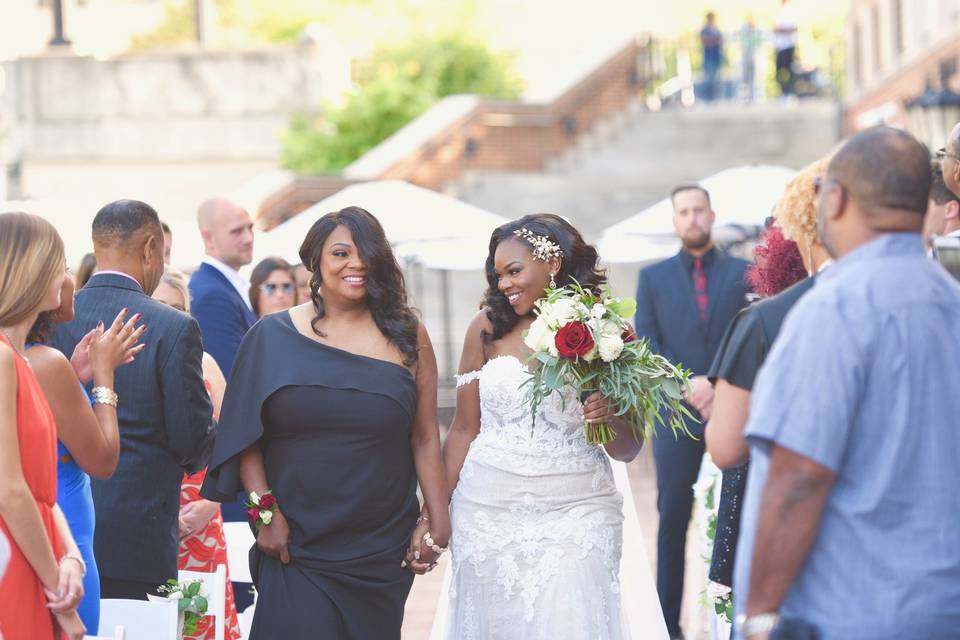 bride smiles as she walks down the ceremony aisle with her mom
