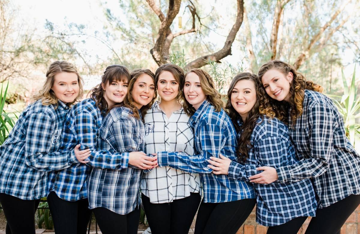 bride wearing white plaid shirt poses with bridesmaids wearing navy blue flannel button downs