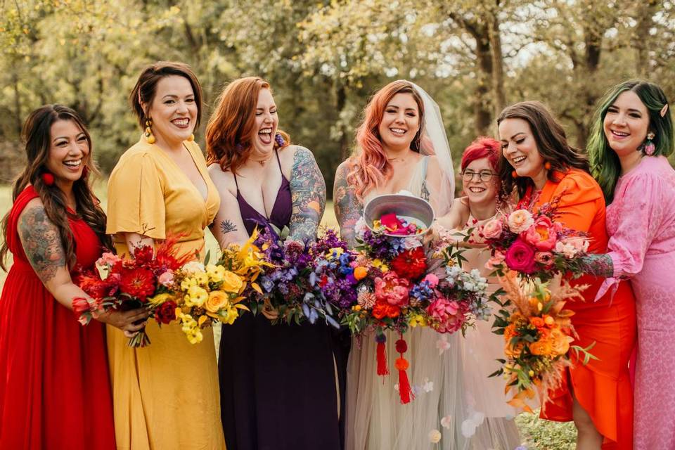 bride stands with her bridesmaids wearing dresses in rainbow colors