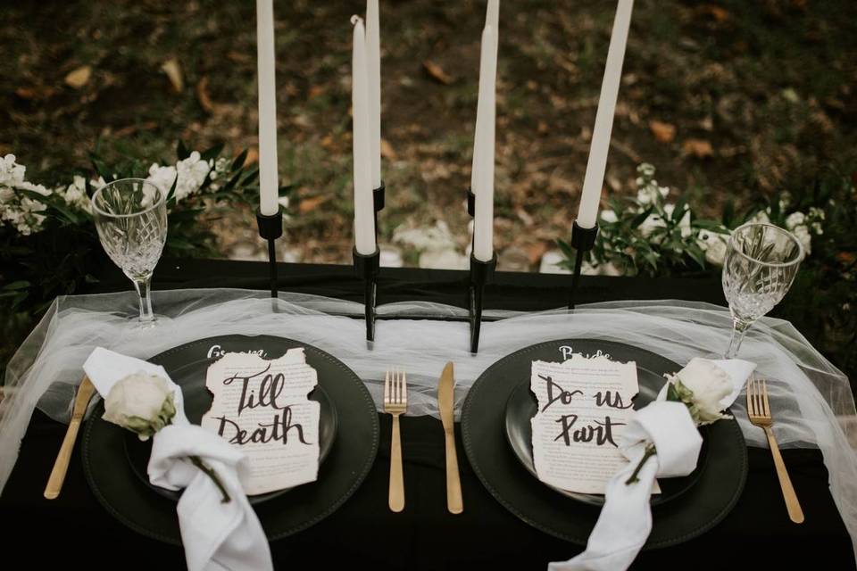 gothic wedding reception tablescape with black plates gold flatware and signs made from book pages that say 