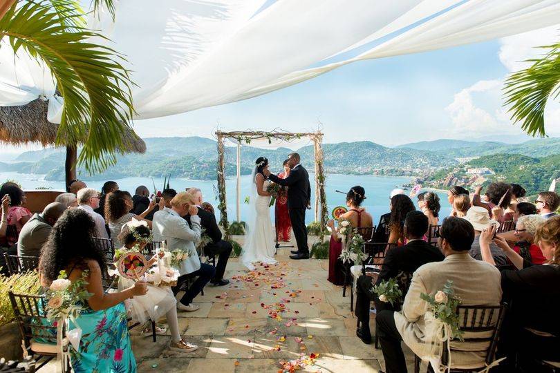 Tropical outdoor wedding with couple standing in front of an arch and guests in seats