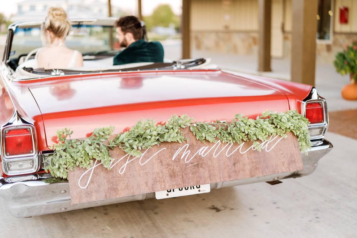 vintage 1960s convertible with wooden "just married" sign decorated with greenery garland on the bumper