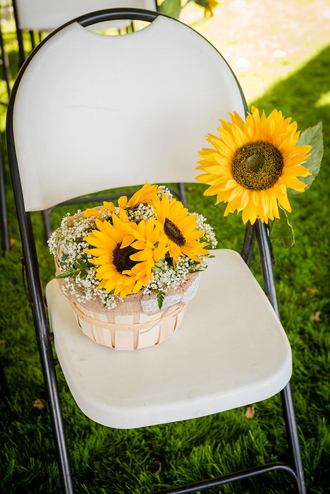 folding chair on grass at outdoor wedding ceremony with a basket of yellow sunflowers and baby's breath