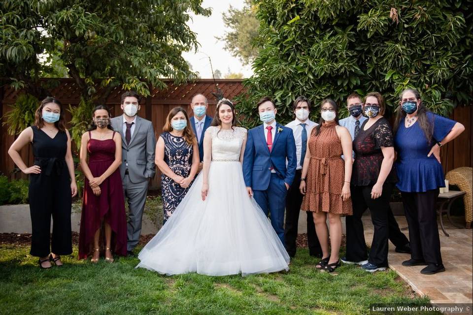 bride and groom stand with family members wearing masks at outdoor wedding venue