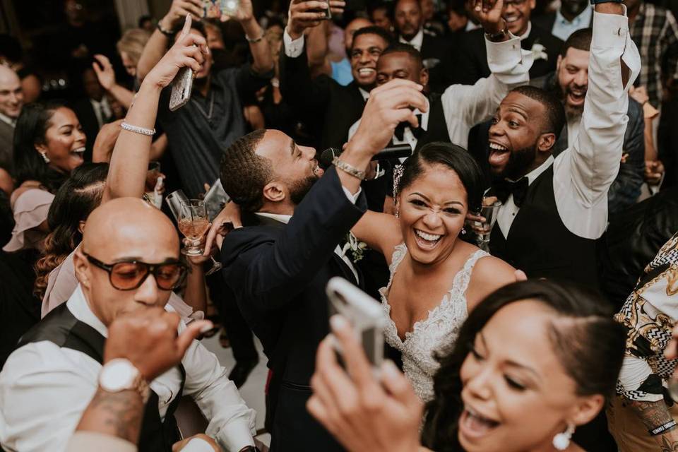 bride and groom are surrounded by smiling guests on the dance floor