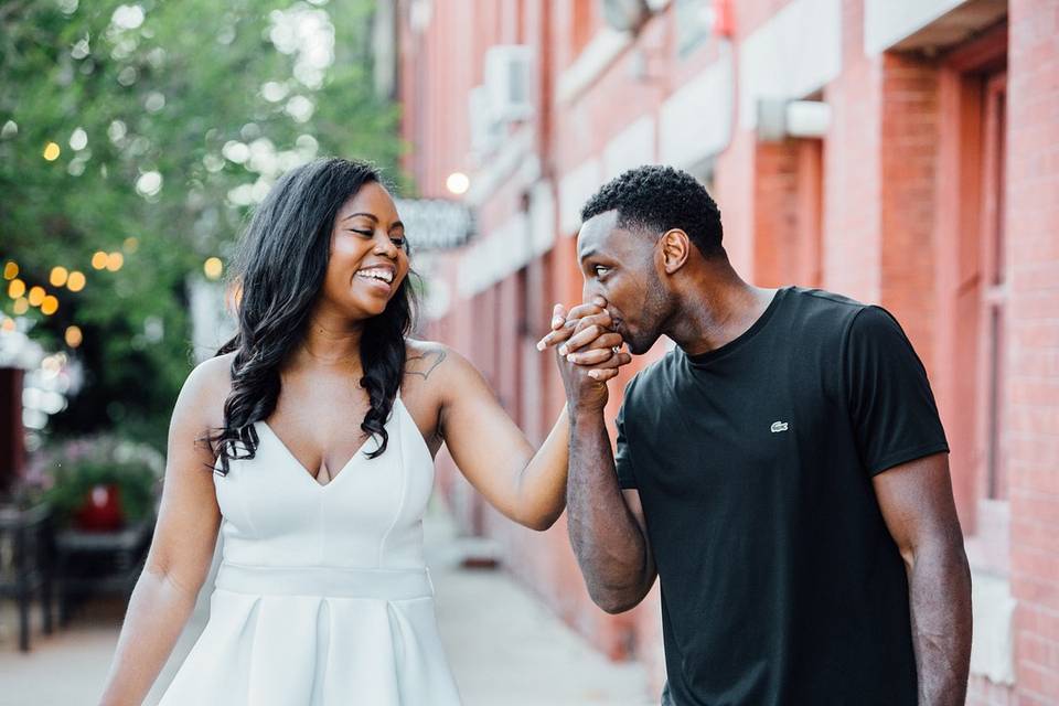 man kisses his fiance's left hand as she looks at him and smiles