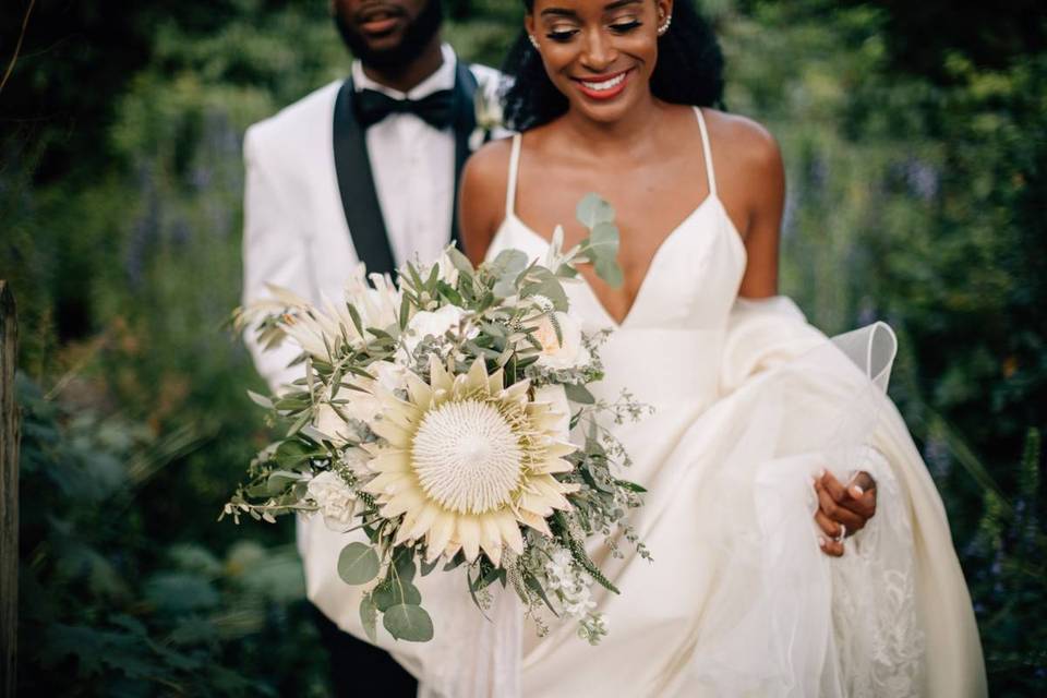 couple walking outside bride holding large protea bouquet