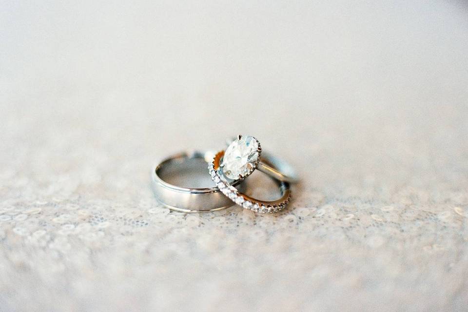 close up of oval solitaire engagement ring with matching pave diamond band and silver men's wedding band