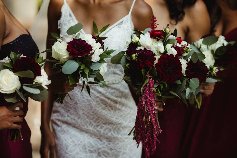 Black bride carries bouquet including burgundy dahlias, red ranunculus, amaranthus, eucalyptus, and other flowers in fall wedding colors