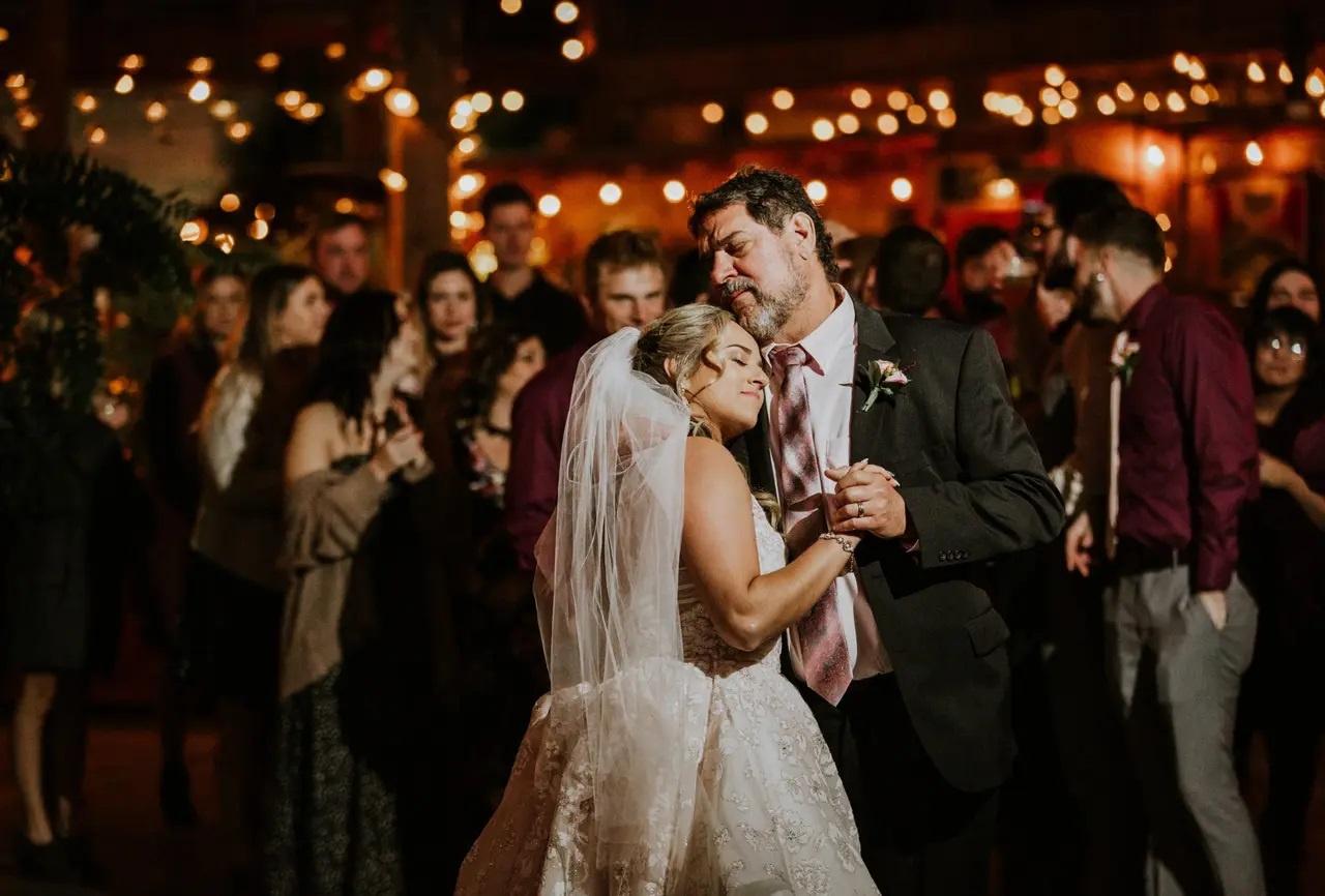 Father daughter dance with guests in background and twinkling lights