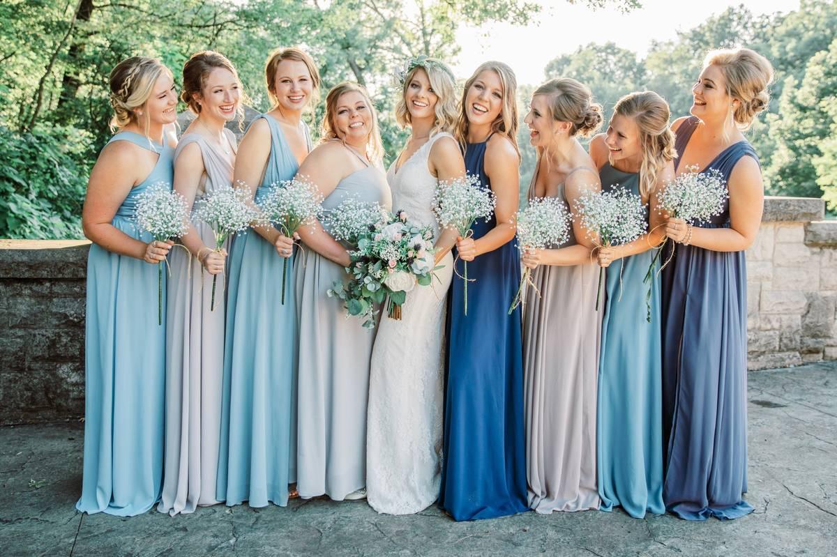 bridesmaids wearing mismatched dresses in light blue colors hold bouquets of baby's breath