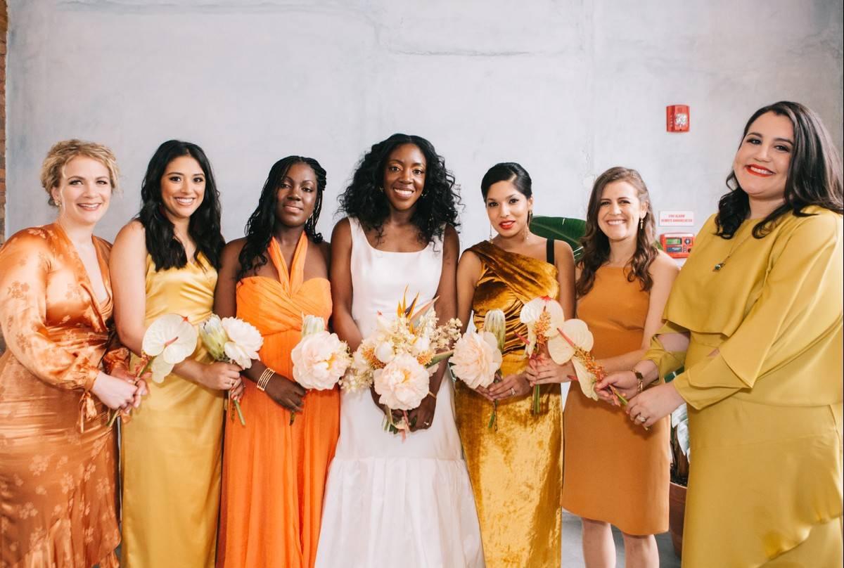 Bride smiling with three bridesmaids either side wearing varying hues of orange and gold