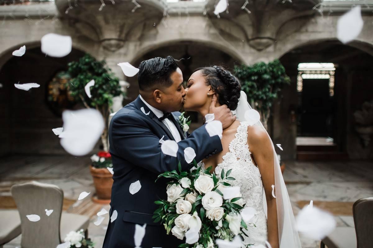 Black bride and groom kissing with rose petals falling around them