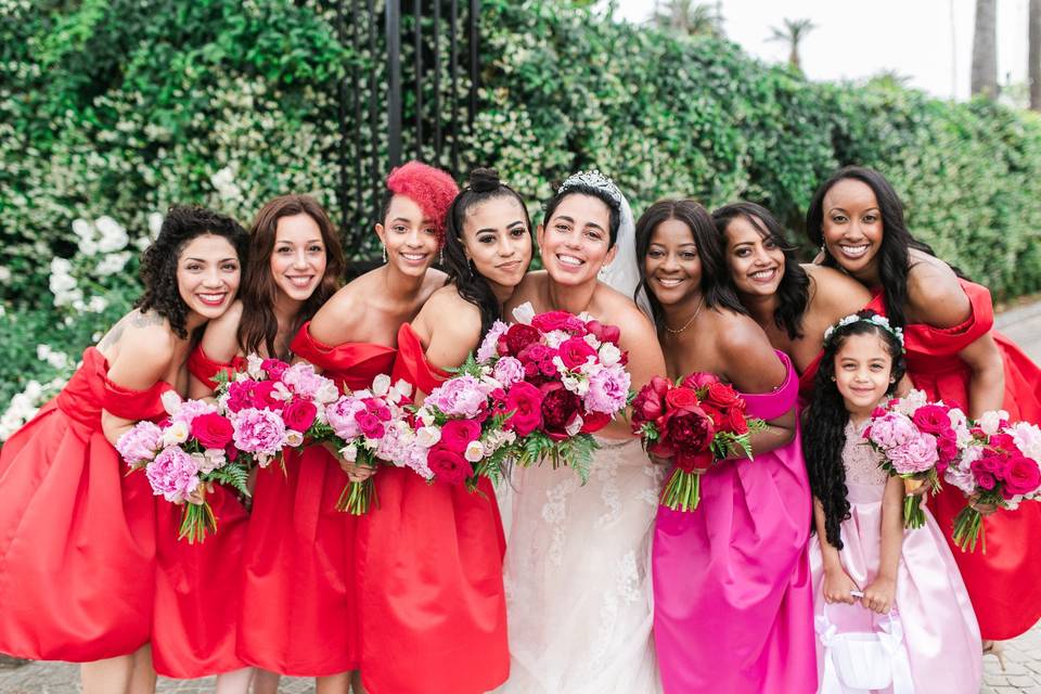 smiling bride poses with her bridesmaids and flower girl holding peony and rose bouquets