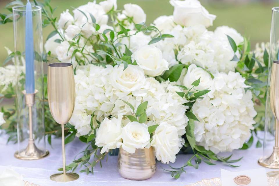 wedding centerpiece with white flowers roses and hydrangeas accented by light blue taper candles and gold champagne flutes