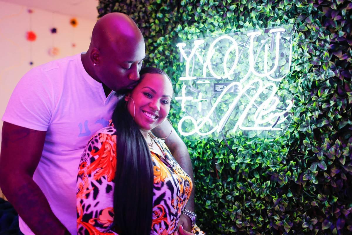 bride and groom stand in front of faux greenery wall with neon sign that says 