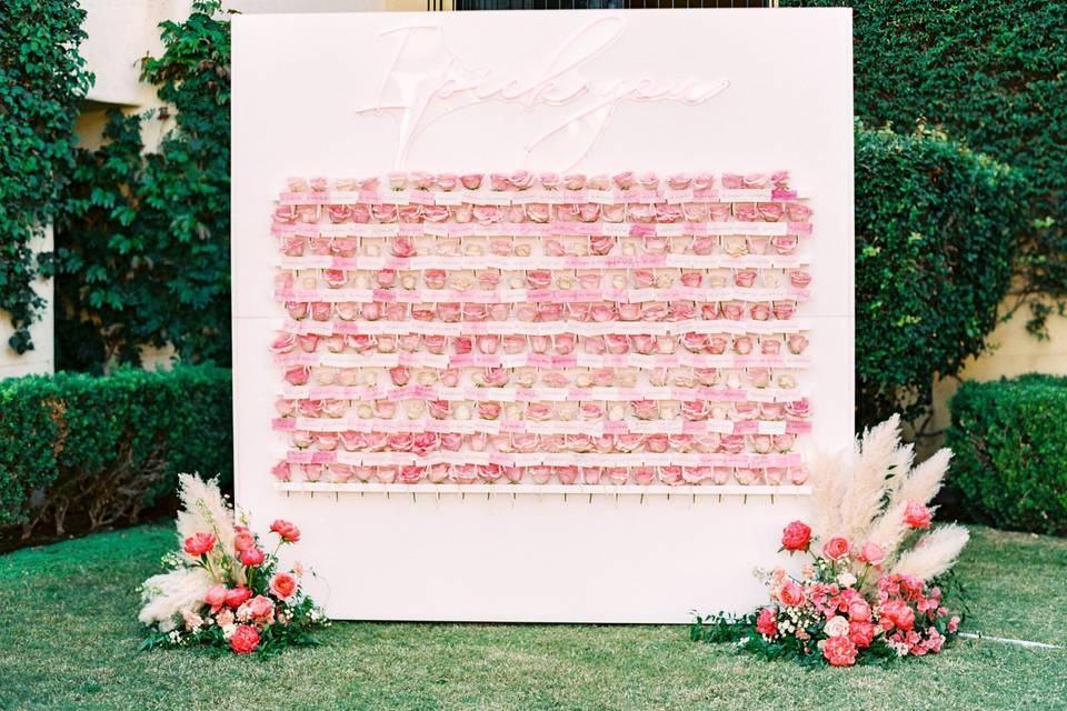 wedding escort card display idea pink wall with individual roses on shelves and 