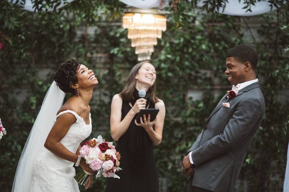 bride and groom stand with their officiant at the altar while laughing