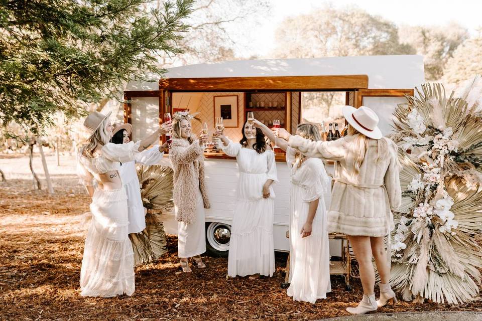 group of women standing outside of a mobile bar clinking champagne glasses