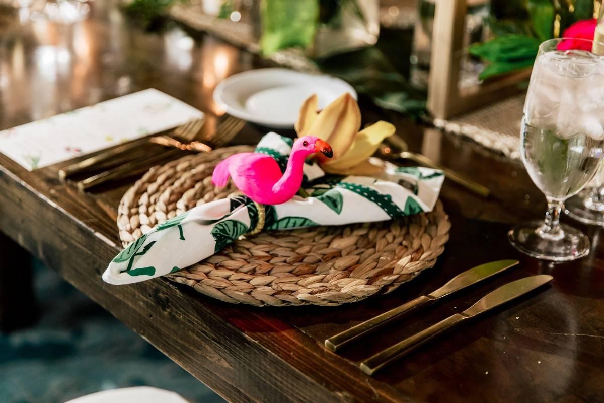 beach wedding place setting with woven rattan charger and flamingo napkin ring with greenery print napkin