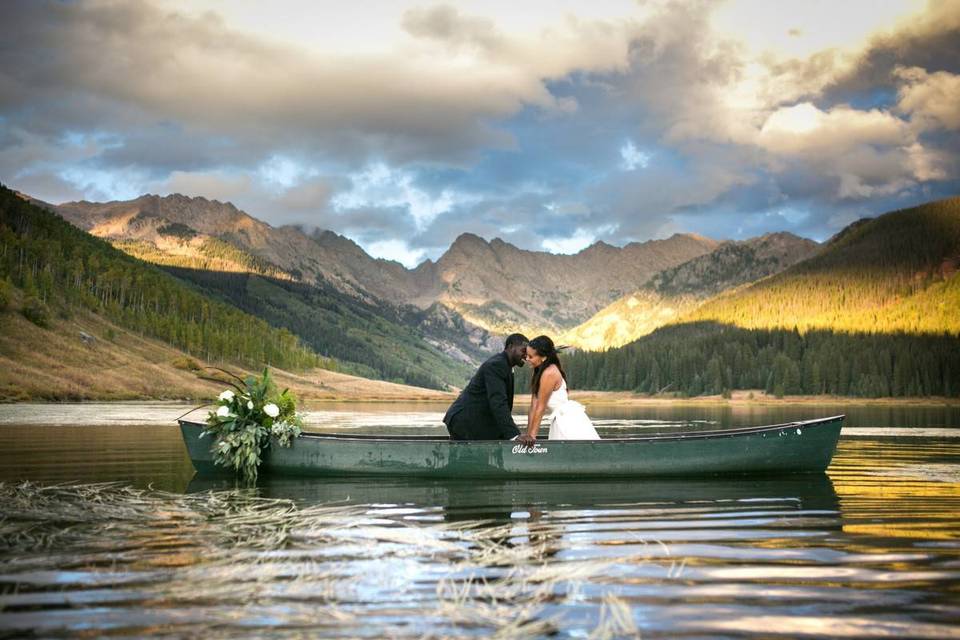 wedding couple sitting in a green canoe with mountains in the background