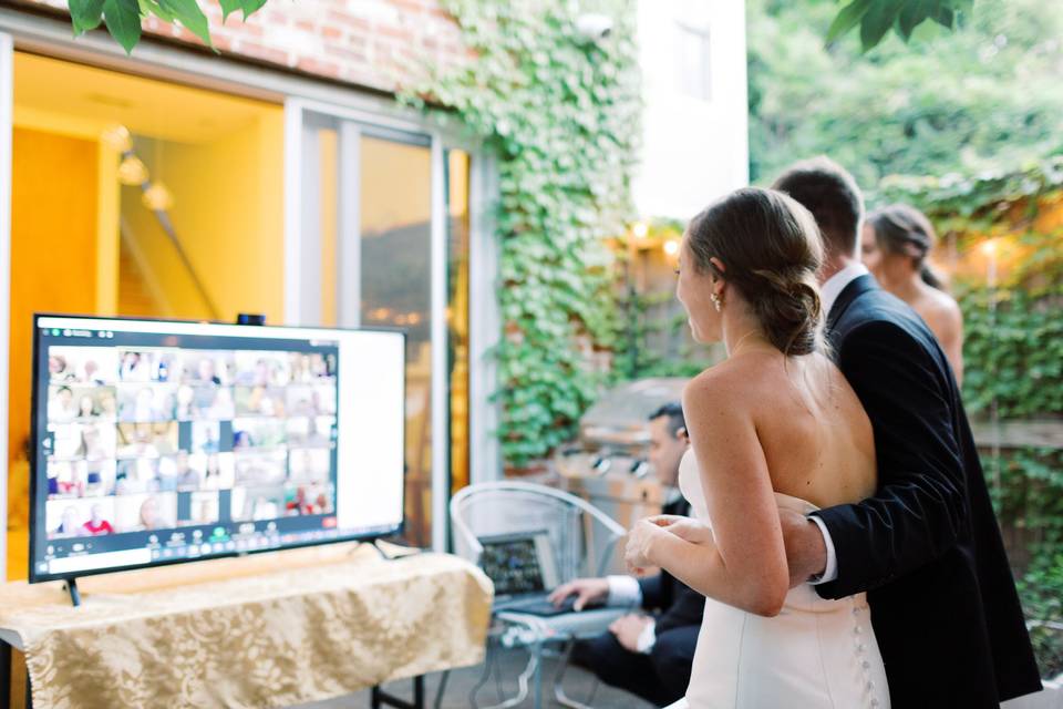 bride and groom looking at a large screen which shows guests via zoom