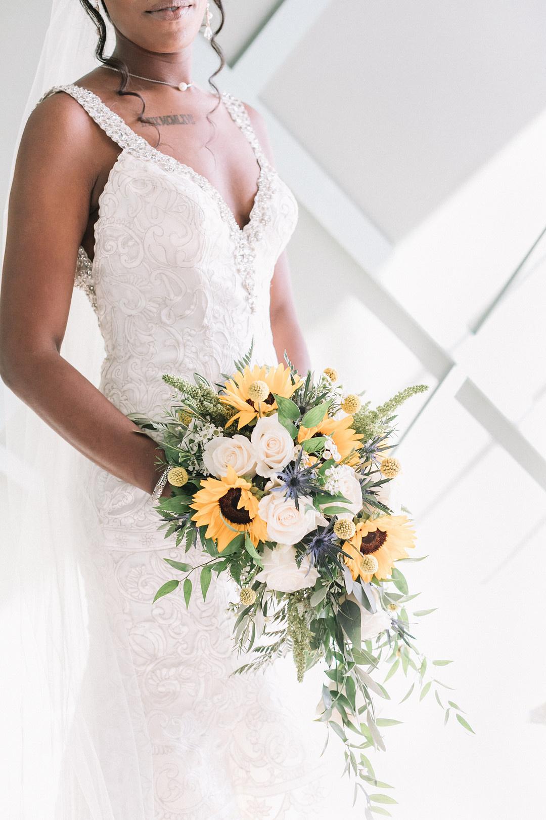 Black bride holds cascading sunflower wedding bouquet with white roses and greenery