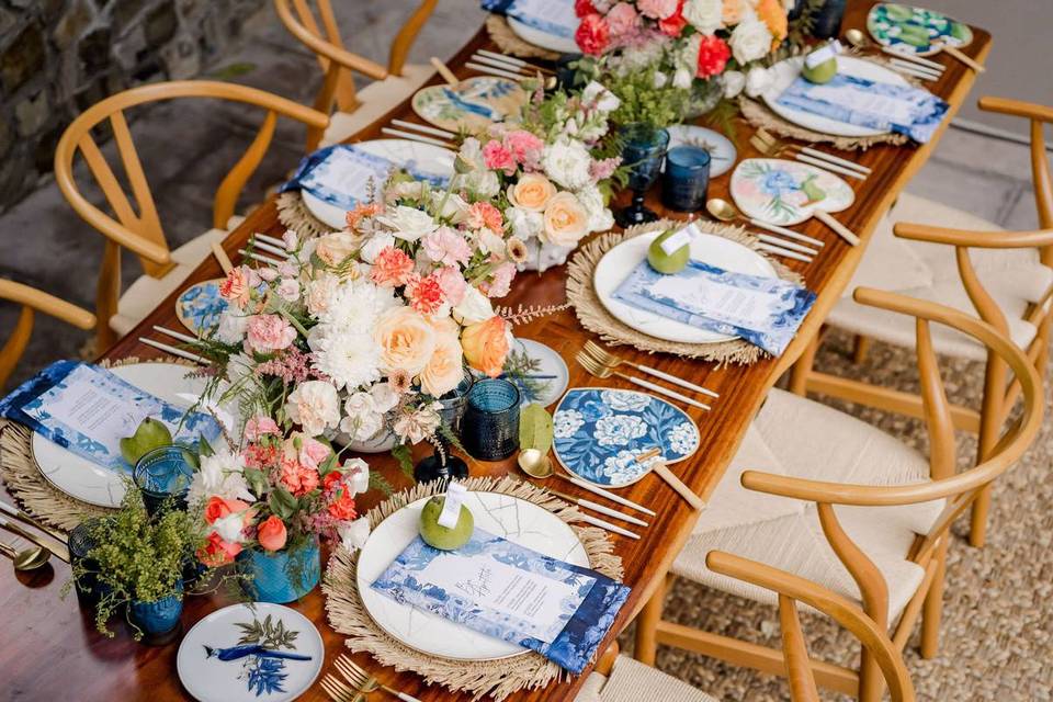 boho wedding tablescape with blue floral print paper fans, rattan place mats, and bright pink and orange centerpieces
