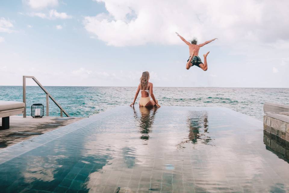 couple jumping from infinity pool into ocean in maldives