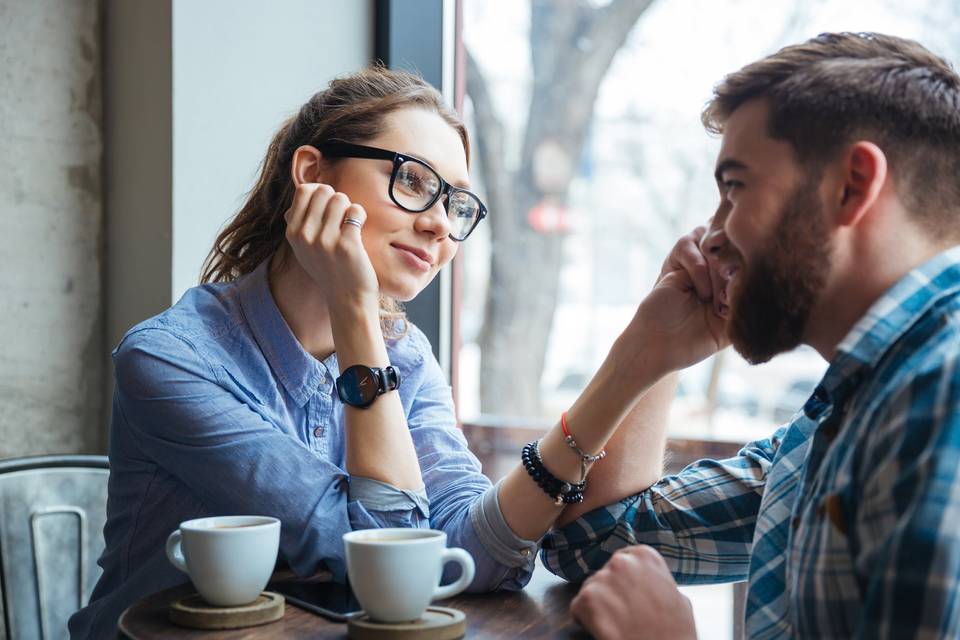 woman and man sitting in a coffee shop looking at each other romantically