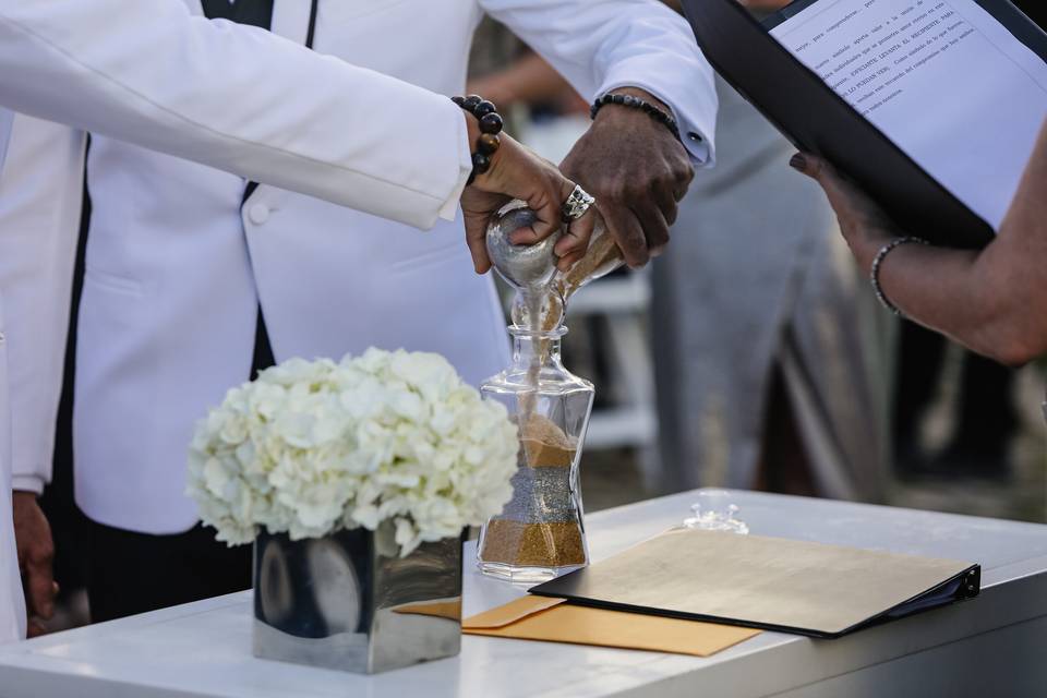 two grooms pour sand into a glass vase