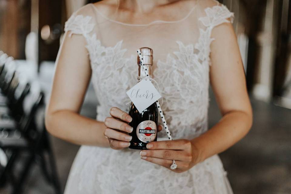 bride holds miniature bottle of rose with polka dot paper straw