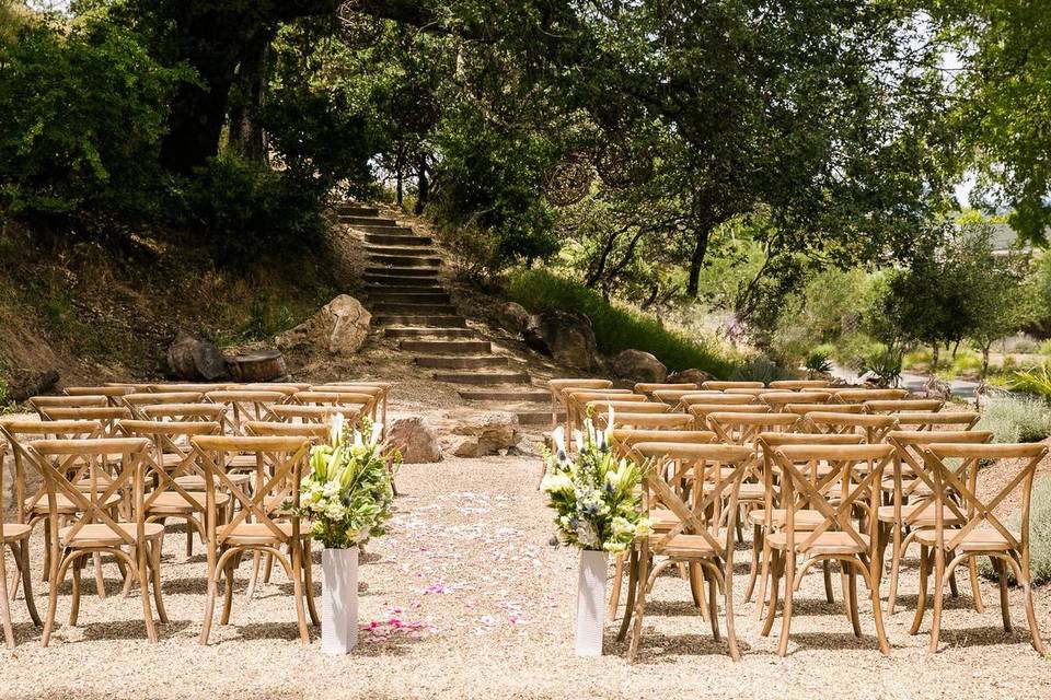 outdoor wedding ceremony at napa venue empty wooden chairs set in rows surrounded by lush green trees