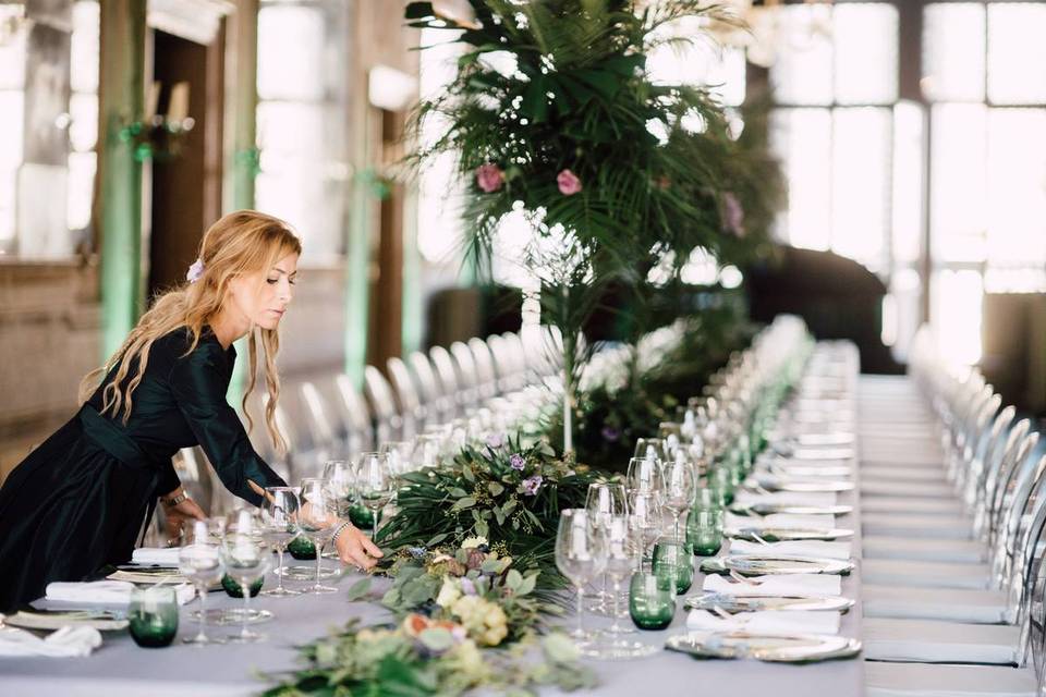 wedding planner leans over table to adjust greenery centerpiece
