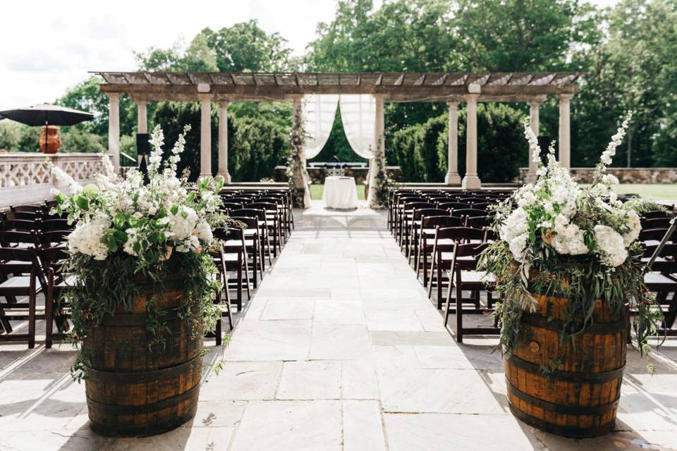wedding prelude songs - outdoor wedding ceremony venue looking toward the altar from the back of the aisle. two wine barrels are placed on either side of the aisle and decorated with fresh flowers on top