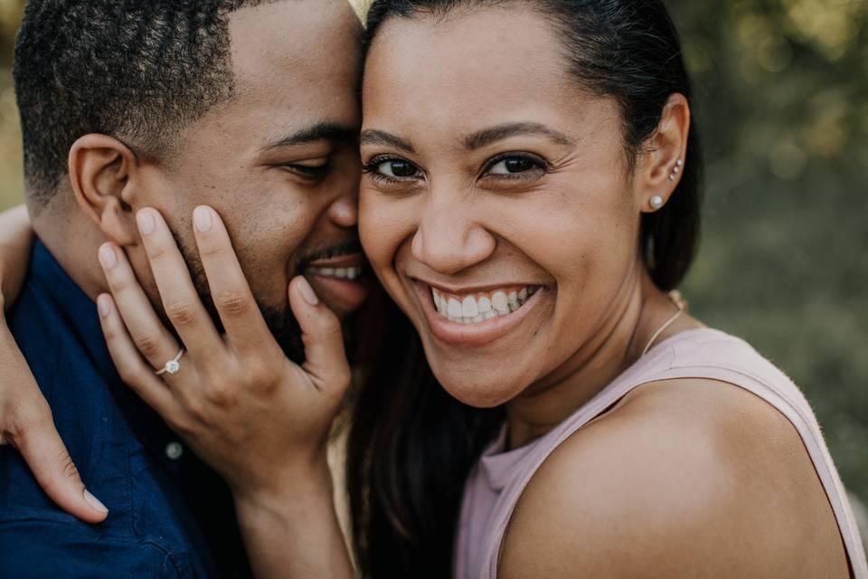 close up portrait of Black couple. she is smiling at the camera while he kisses her cheek
