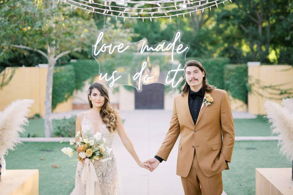 bride and groom standing in front of a neon sign that says love made us do it