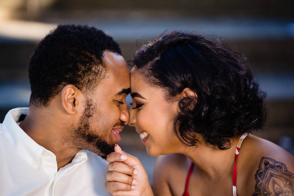 side portrait of a black couple smiling and pressing foreheads together, she has her hand on his chin