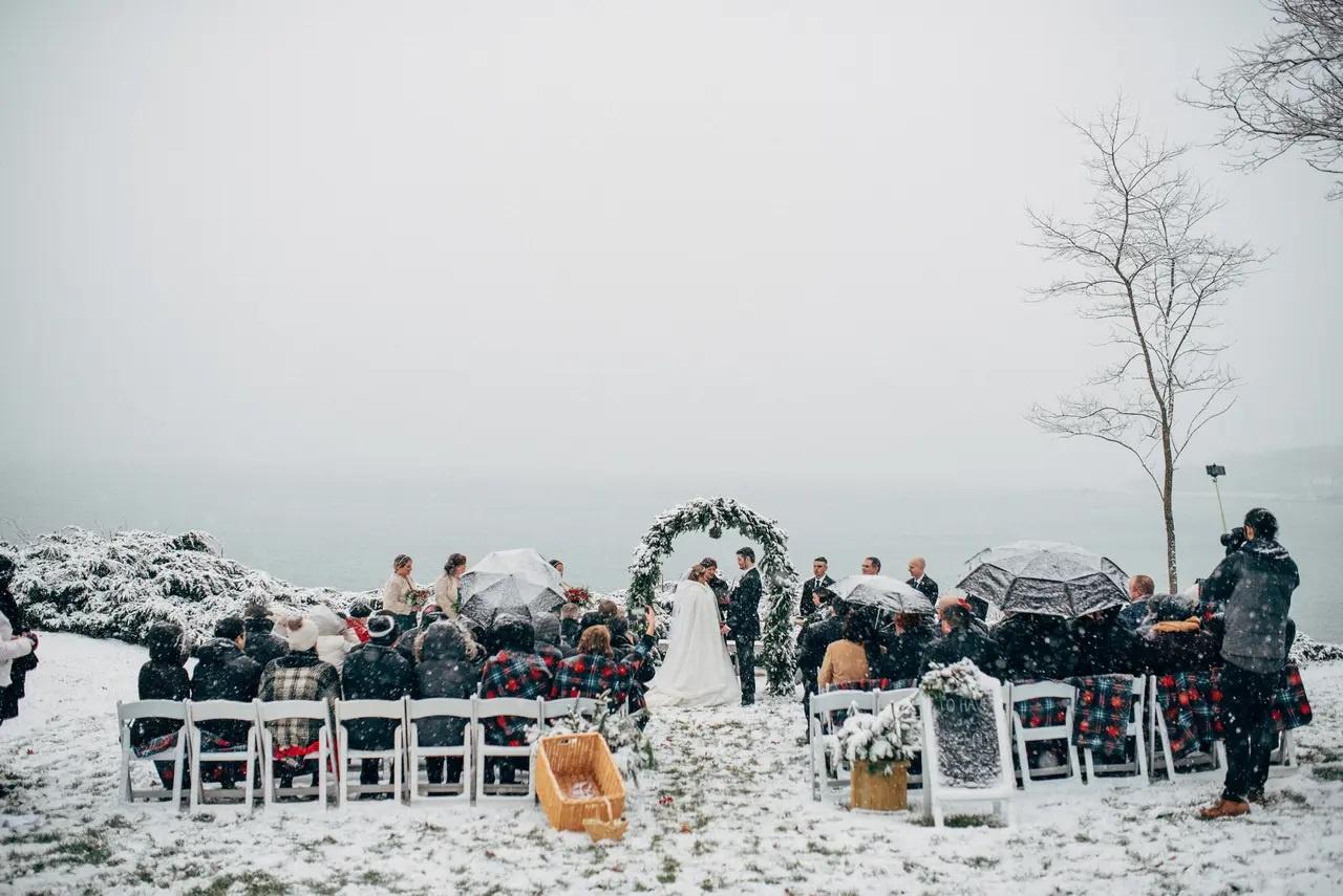 Snowy winter wedding ceremony outdoors with guests wearing plaid blankets