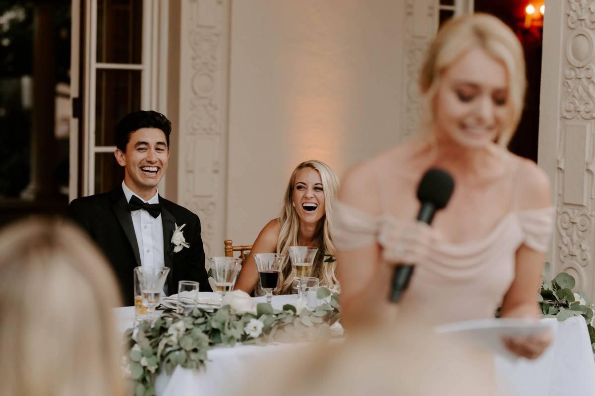 bride and groom laugh hysterically while maid of honor gives a speech