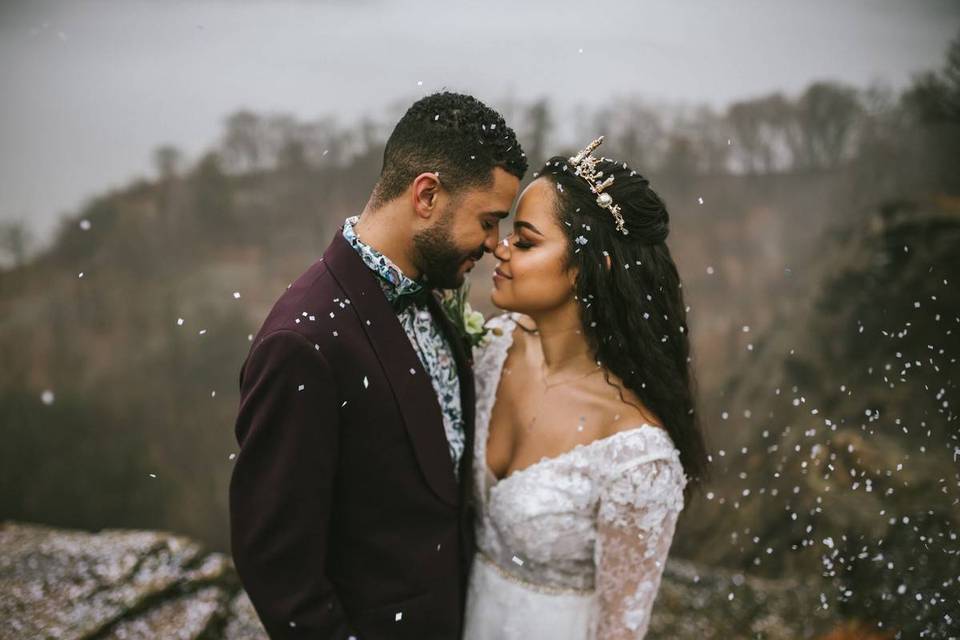 Bride and groom stand face to face with their eyes closed as they are showered with white confetti