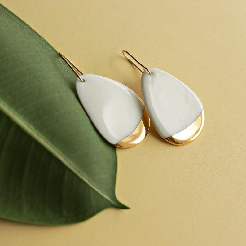 white and gold drop earrings set against a leaf backdrop