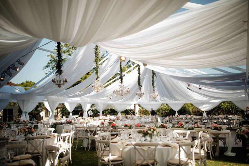 tented wedding decorated with white draped fabrics chandeliers and greenery